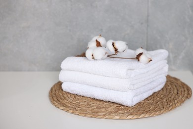 Photo of Clean towels and cotton flowers on white table indoors, closeup. Space for text