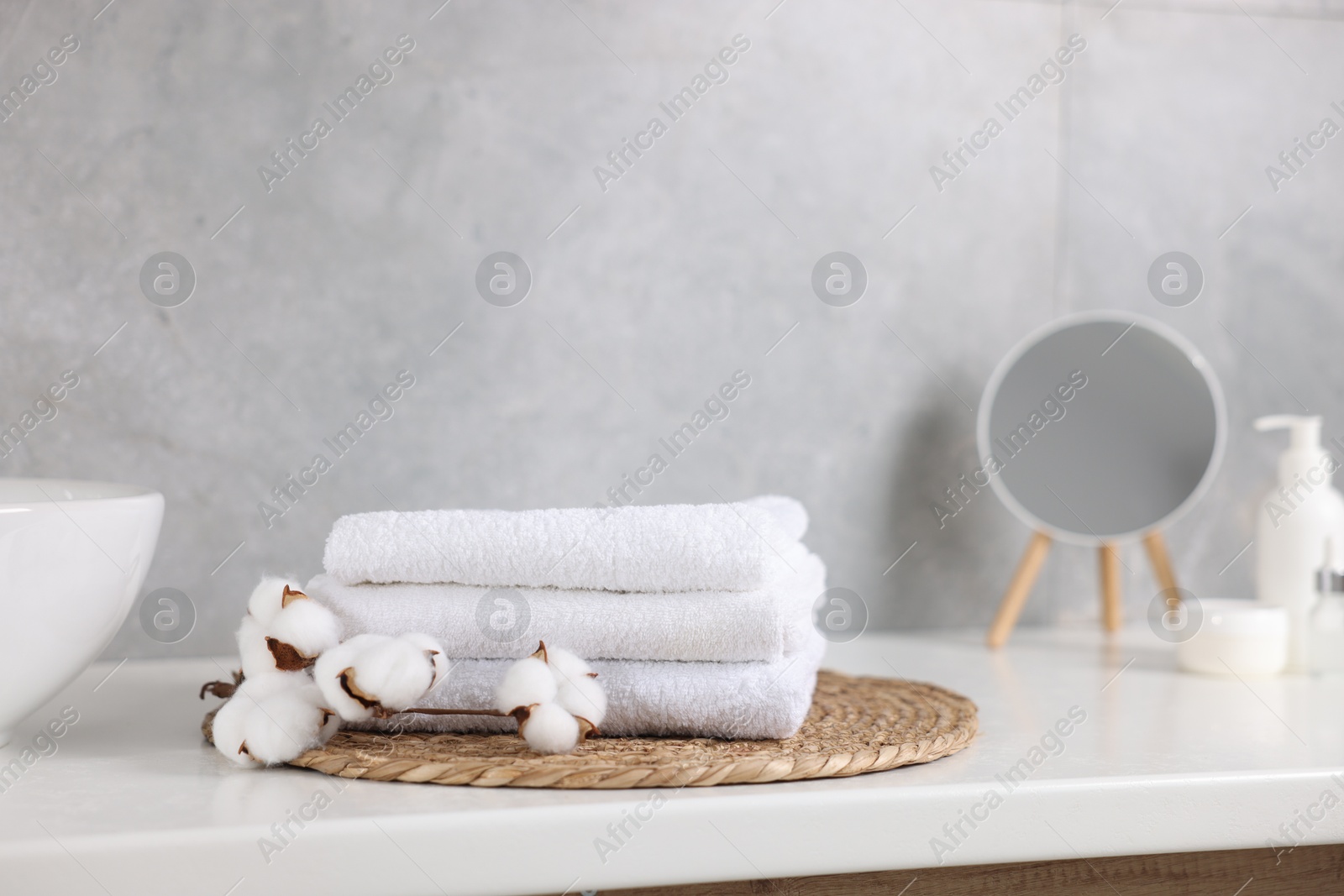 Stack of clean towels, cotton flowers, cosmetic products and mirror on vanity indoors Photo of Stack of clean towels, cotton flowers, cosmetic products and mirror on vanity indoors