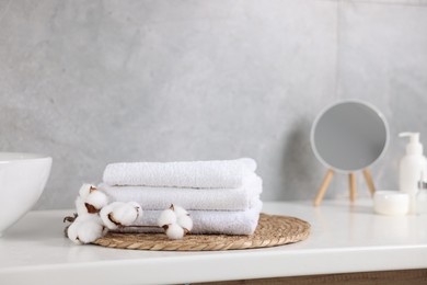 Photo of Stack of clean towels, cotton flowers, cosmetic products and mirror on vanity indoors