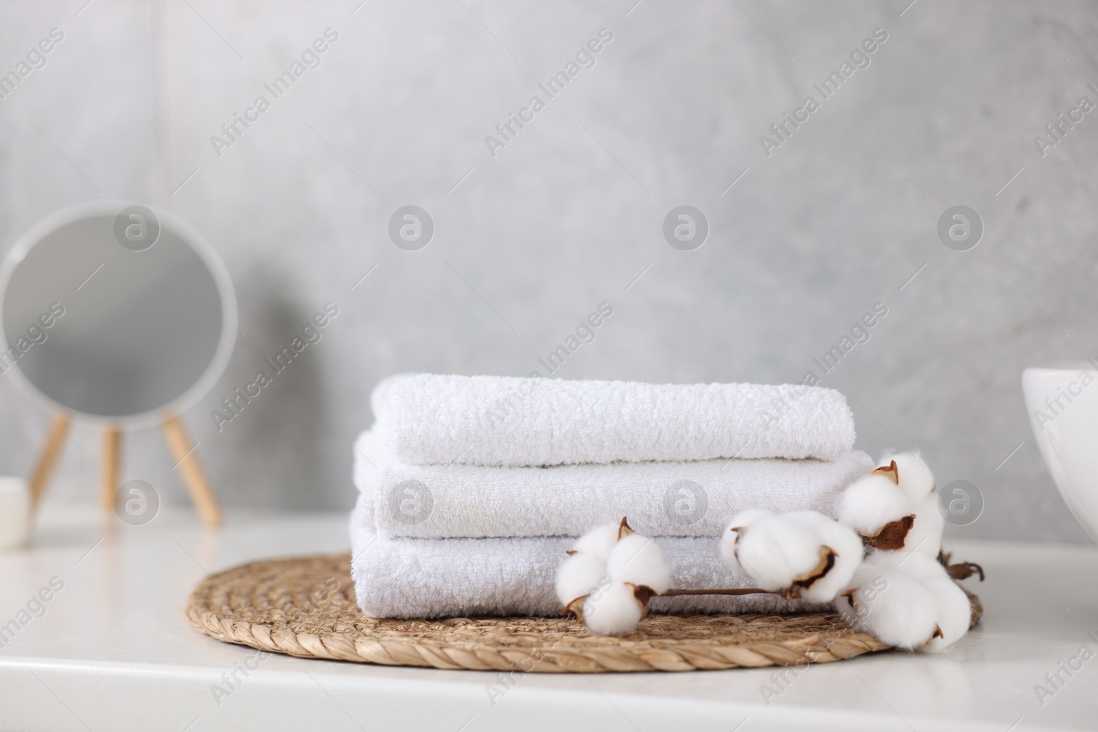 Stack of clean towels, cotton flowers and mirror on white table indoors, closeup Photo of Stack of clean towels, cotton flowers and mirror on white table indoors, closeup