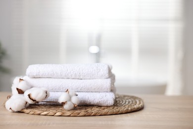 Photo of Stack of clean towels and cotton flowers on wooden table indoors, closeup. Space for text