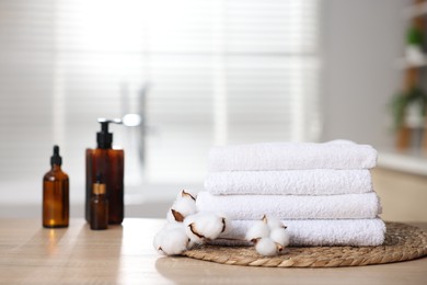 Photo of Stack of clean towels, cotton flowers and cosmetic products on wooden table indoors