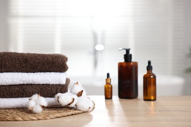 Photo of Stack of clean towels, cotton flowers and cosmetic products on wooden table indoors, closeup