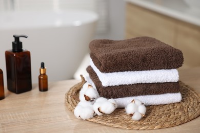 Photo of Stack of clean towels, cotton flowers and cosmetic products on wooden table indoors, closeup