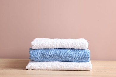 Photo of Stack of clean towels on wooden table against beige background, closeup
