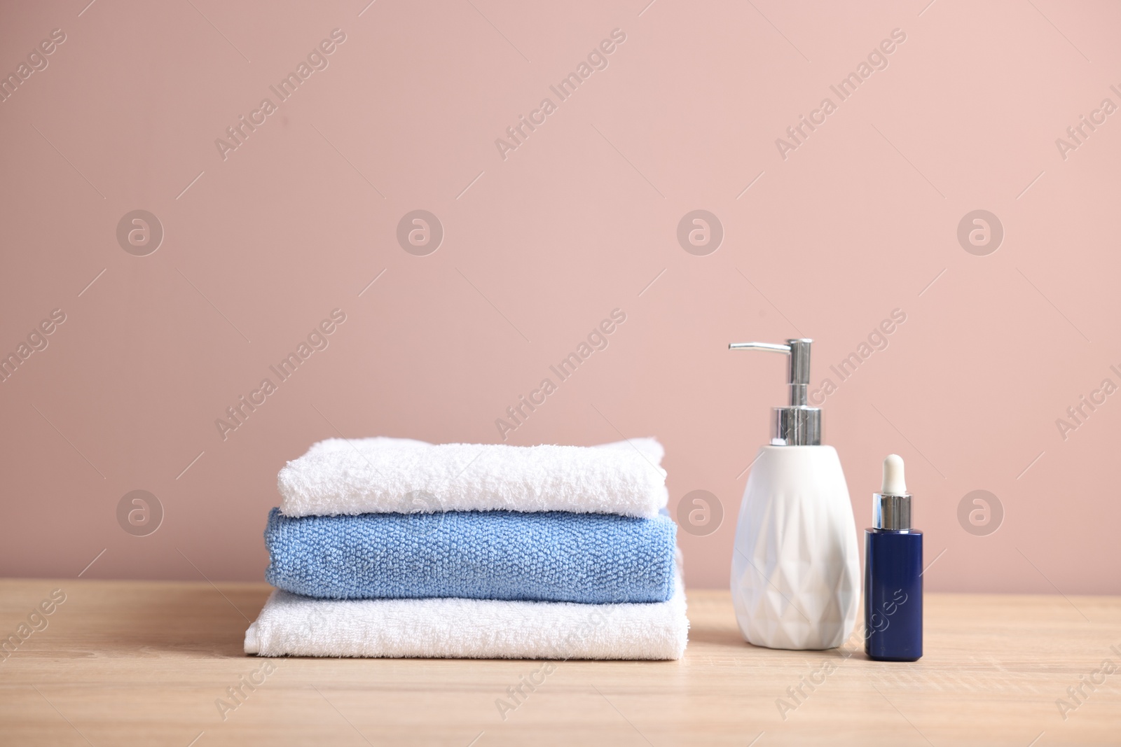 Stack of clean towels and cosmetic products on wooden table against beige background Photo of Stack of clean towels and cosmetic products on wooden table against beige background