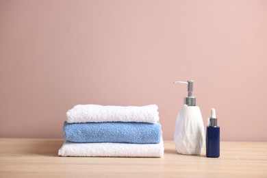 Photo of Stack of clean towels and cosmetic products on wooden table against beige background