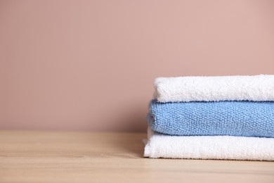Photo of Stack of clean towels on wooden table against beige background, closeup. Space for text