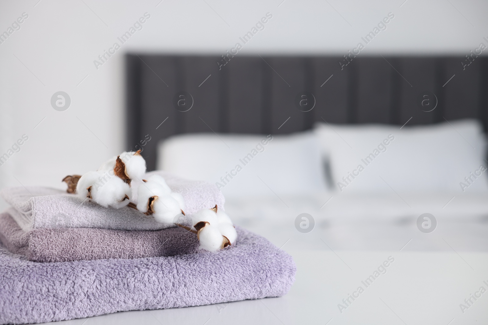 Clean terry towels and cotton flowers on bed at home, closeup. Space for text Photo of Clean terry towels and cotton flowers on bed at home, closeup. Space for text