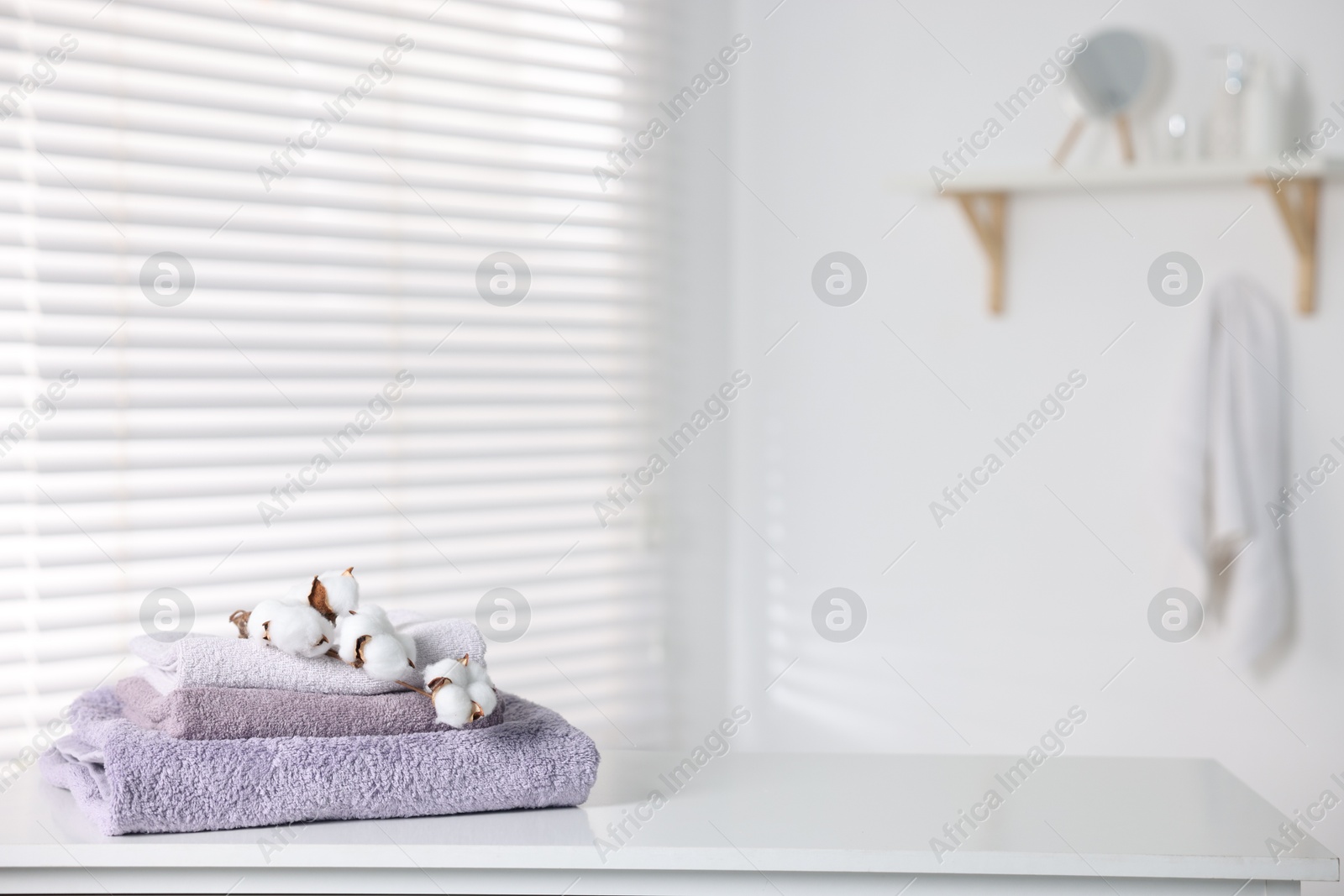 Clean terry towels and cotton flowers on white table in bathroom, space for text Photo of Clean terry towels and cotton flowers on white table in bathroom, space for text
