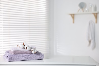 Photo of Clean terry towels and cotton flowers on white table in bathroom, space for text