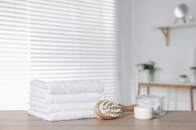 Photo of Clean terry towels, brush, cosmetic product, swabs on wooden table in bathroom