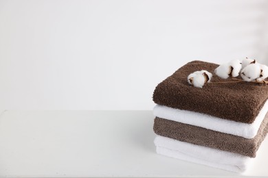 Photo of Stack of clean towels and cotton flowers on white table. Space for text
