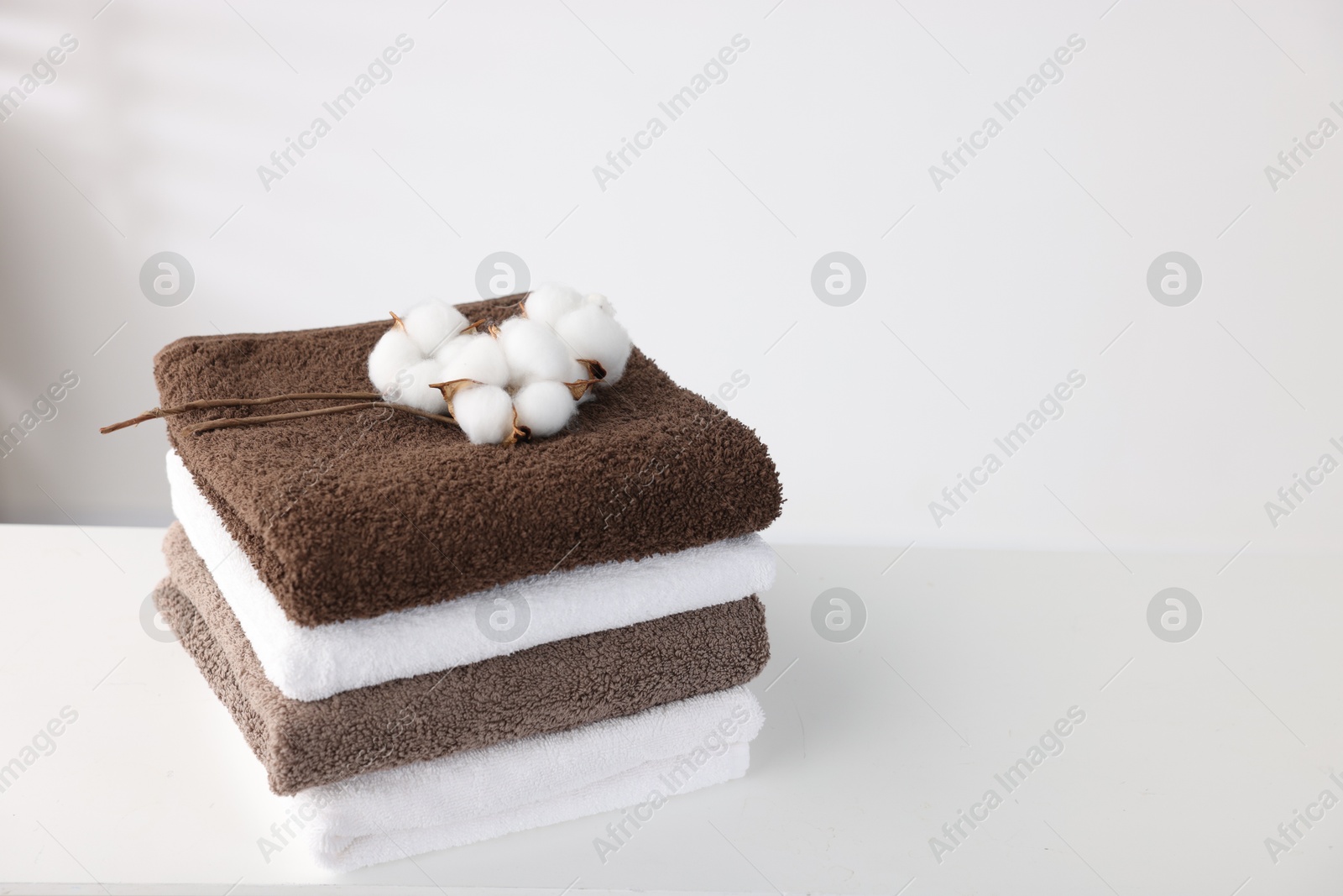 Stack of clean towels and cotton flowers on white table. Space for text Photo of Stack of clean towels and cotton flowers on white table. Space for text