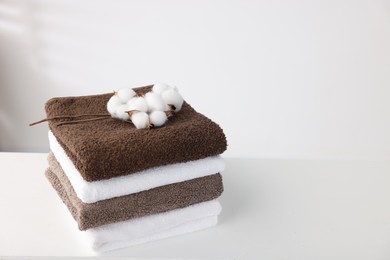 Photo of Stack of clean towels and cotton flowers on white table. Space for text