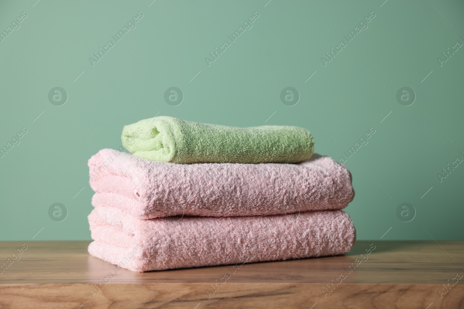 Stack of clean towels on wooden table against green background, closeup Photo of Stack of clean towels on wooden table against green background, closeup