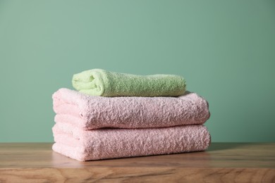 Photo of Stack of clean towels on wooden table against green background, closeup