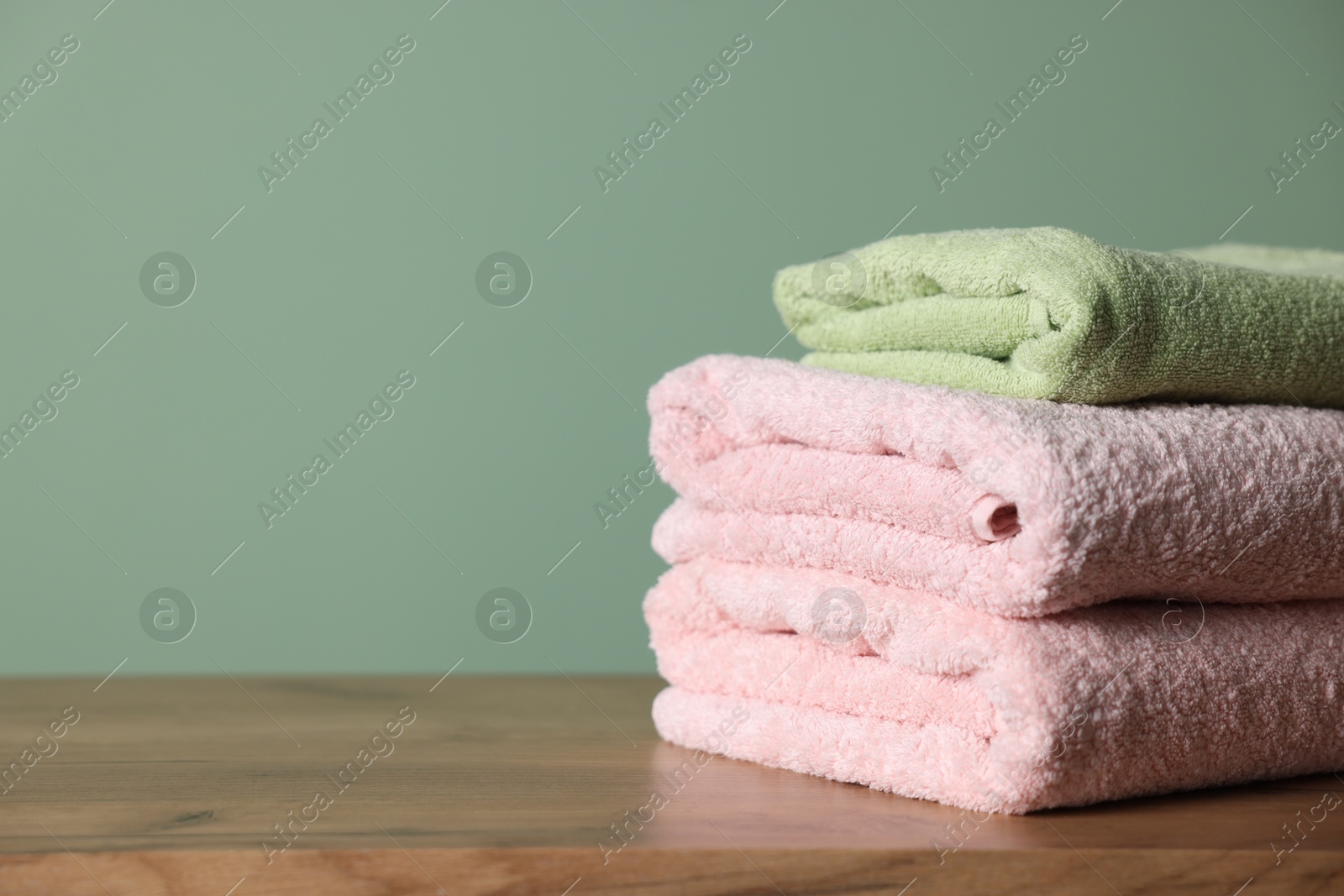 Stack of clean towels on wooden table against green background, closeup. Space for text Photo of Stack of clean towels on wooden table against green background, closeup. Space for text