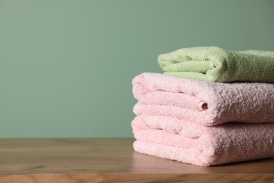 Photo of Stack of clean towels on wooden table against green background, closeup. Space for text