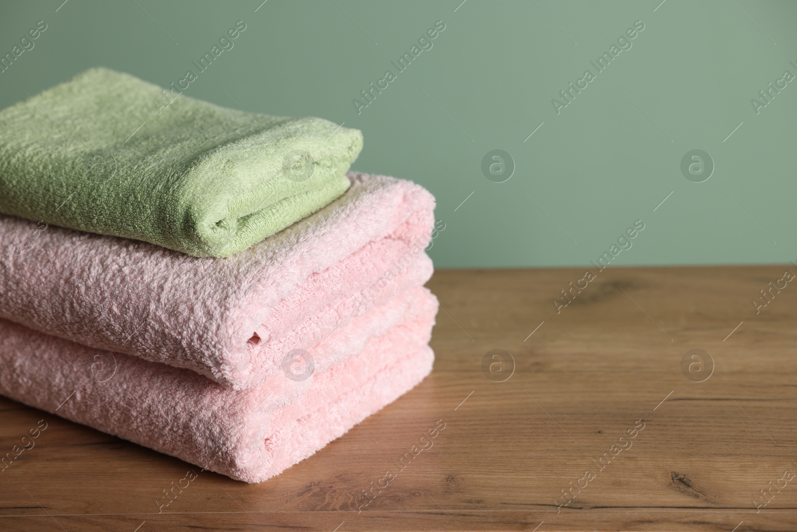 Stack of clean towels on wooden table against green background, closeup. Space for text Photo of Stack of clean towels on wooden table against green background, closeup. Space for text