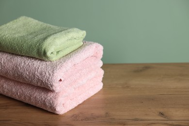 Photo of Stack of clean towels on wooden table against green background, closeup. Space for text