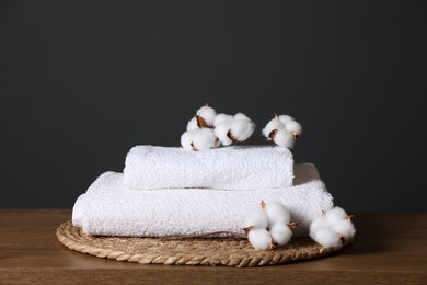 Photo of Stack of clean towels and cotton flowers on wooden table against dark grey background