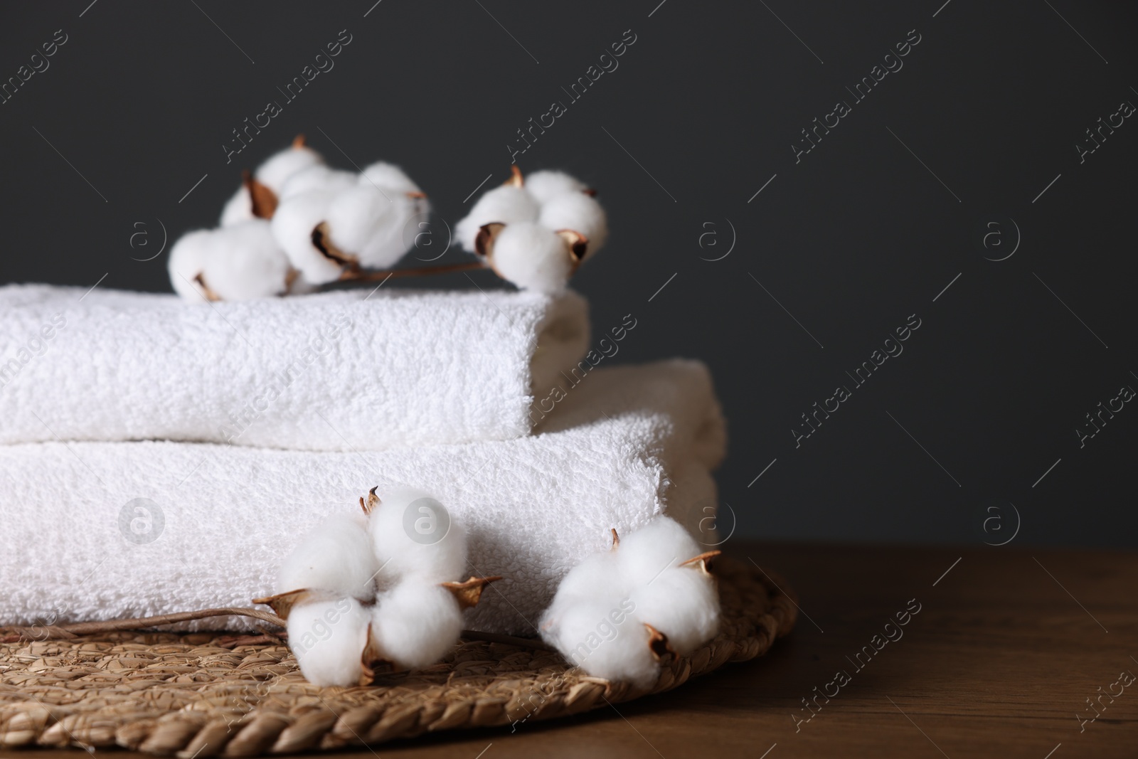 Stack of clean towels and cotton flowers on wooden table against dark grey background, closeup. Space for text Photo of Stack of clean towels and cotton flowers on wooden table against dark grey background, closeup. Space for text