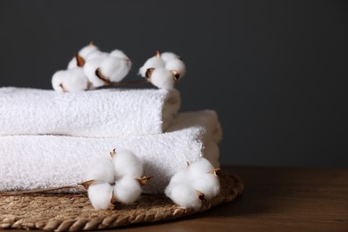 Photo of Stack of clean towels and cotton flowers on wooden table against dark grey background, closeup. Space for text