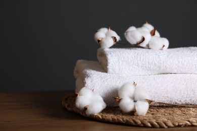 Photo of Stack of clean towels and cotton flowers on wooden table against dark grey background, closeup. Space for text