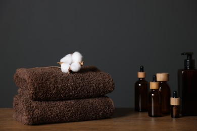 Photo of Stack of clean towels, cotton flower and cosmetic products on wooden table against dark grey background