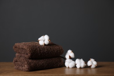 Photo of Stack of clean towels and cotton flowers on wooden table against dark grey background