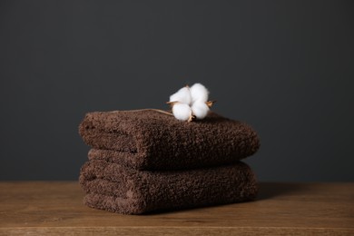 Photo of Stack of clean towels and cotton flower on wooden table against dark grey background, closeup