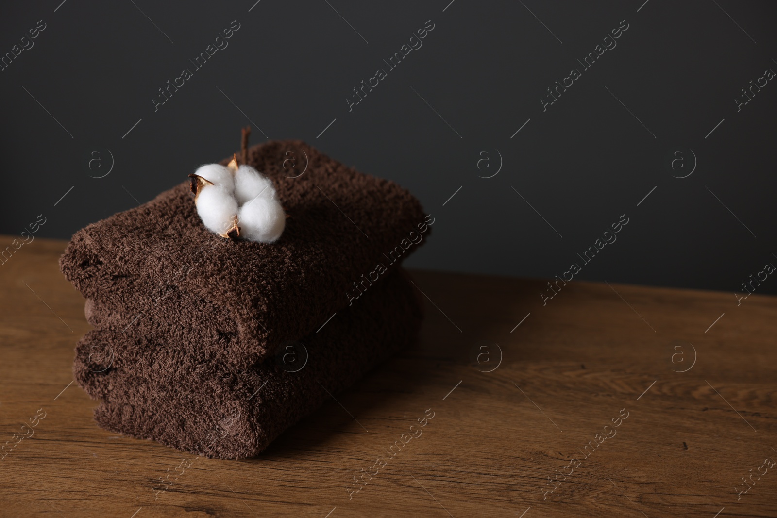 Stack of clean towels and cotton flower on wooden table against dark grey background, closeup. Space for text Photo of Stack of clean towels and cotton flower on wooden table against dark grey background, closeup. Space for text