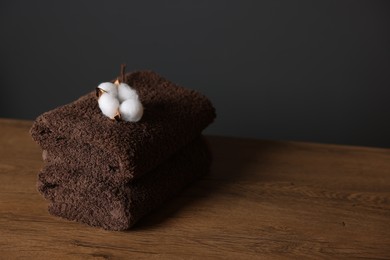 Photo of Stack of clean towels and cotton flower on wooden table against dark grey background, closeup. Space for text