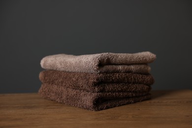 Photo of Stack of clean towels on wooden table against dark grey background, closeup
