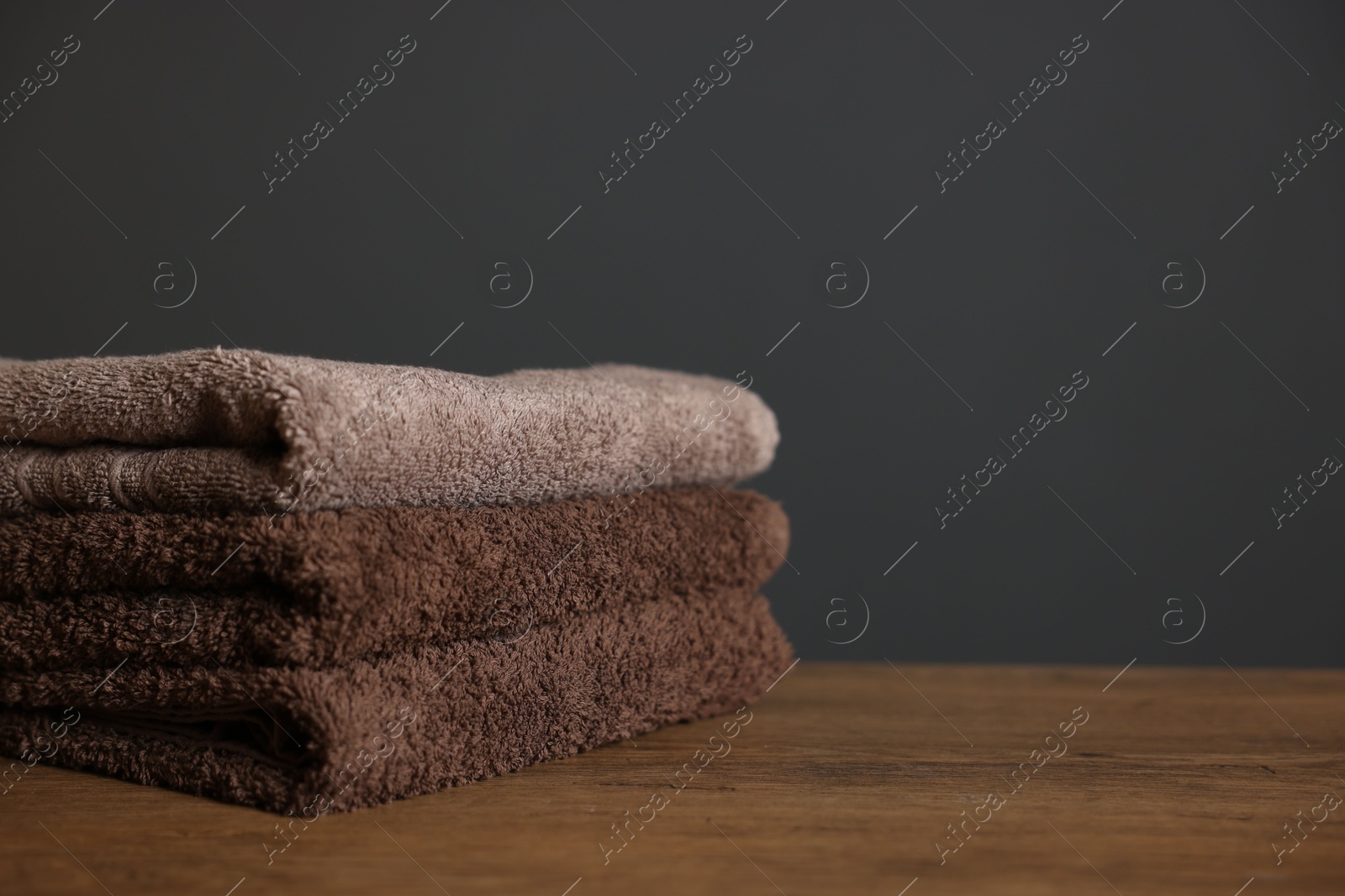 Stack of clean towels on wooden table against dark grey background, closeup. Space for text Photo of Stack of clean towels on wooden table against dark grey background, closeup. Space for text