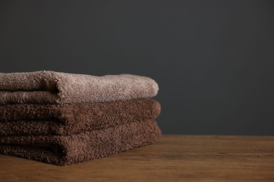 Photo of Stack of clean towels on wooden table against dark grey background, closeup. Space for text