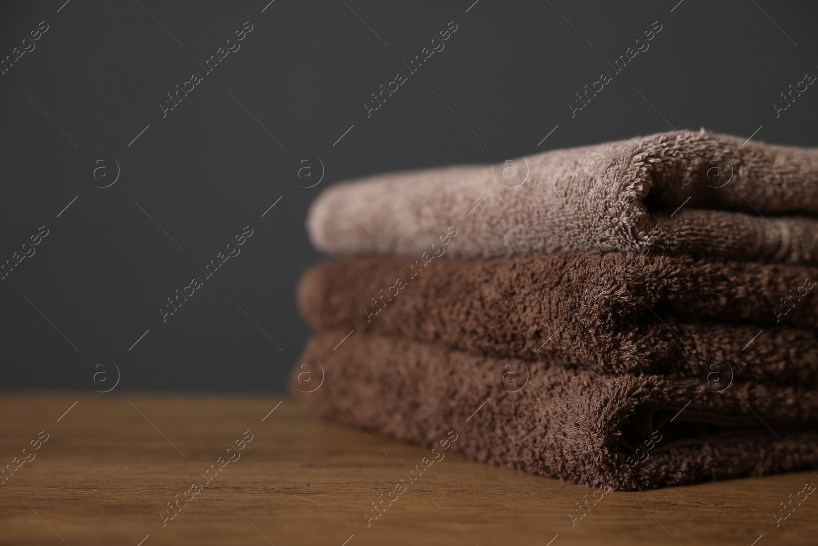 Stack of clean towels on wooden table against dark grey background, closeup. Space for text Photo of Stack of clean towels on wooden table against dark grey background, closeup. Space for text