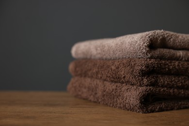 Photo of Stack of clean towels on wooden table against dark grey background, closeup. Space for text