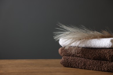 Photo of Stack of clean towels and decor on wooden table against dark grey background, closeup. Space for text