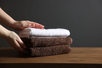 Photo of Woman with clean towels at wooden table against dark grey background, closeup