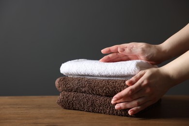 Photo of Woman with clean towels at wooden table against dark grey background, closeup