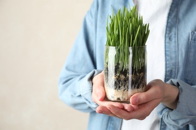 Photo of Woman with wheat grass in transparent pot on light background, closeup. Space for text