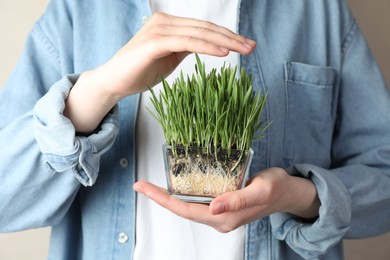 Photo of Woman with wheat grass in transparent pot on light background, closeup