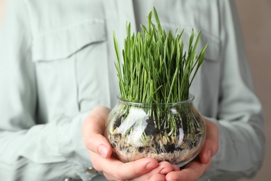 Photo of Woman with wheat grass in transparent pot on light background, closeup