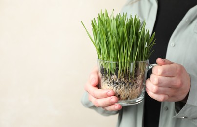 Photo of Woman with wheat grass in transparent pot on light background, closeup. Space for text