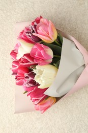Photo of Bouquet of beautiful tulips on white textured table, top view