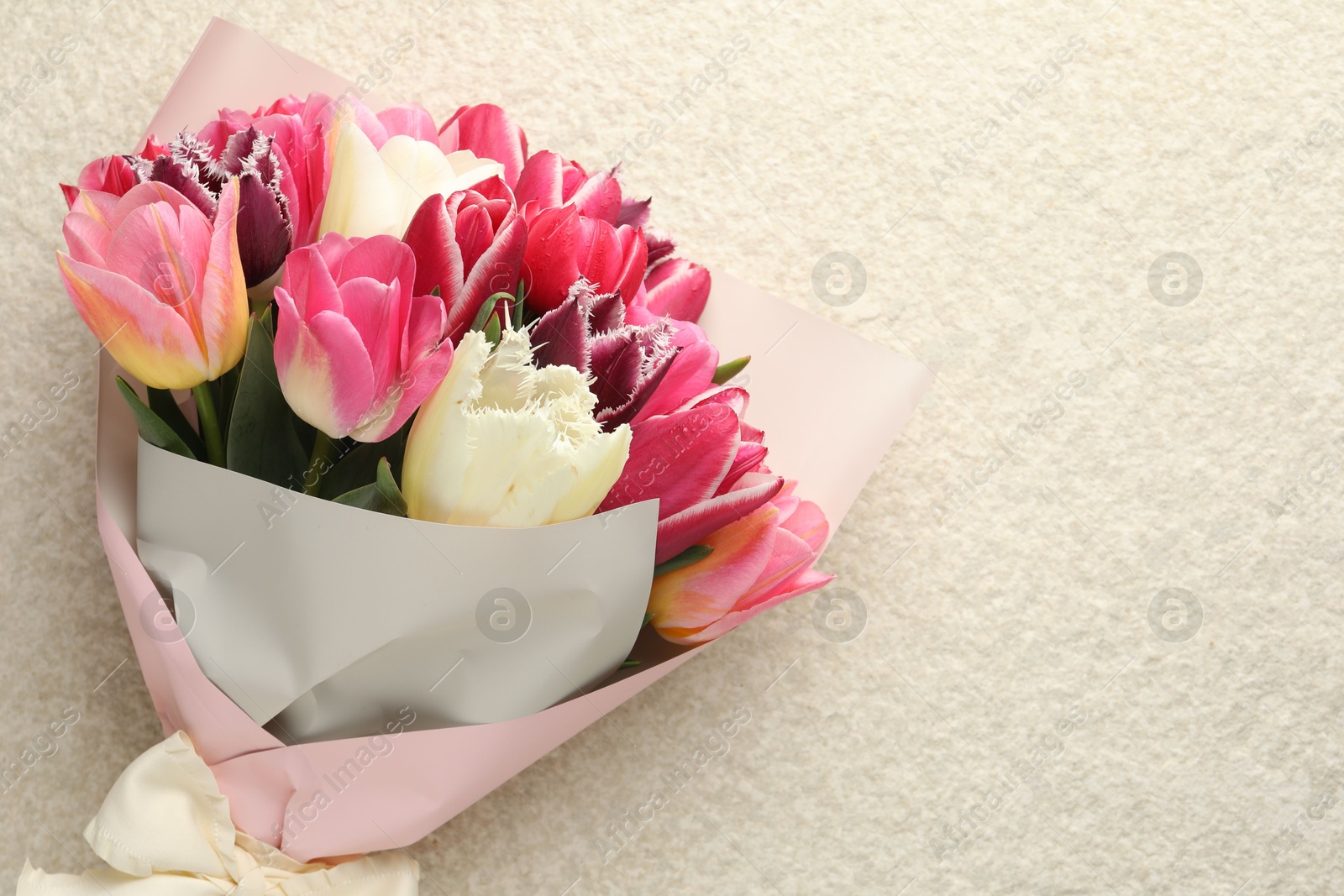 Bouquet of beautiful tulips on white textured table, top view. Space for text Photo of Bouquet of beautiful tulips on white textured table, top view. Space for text