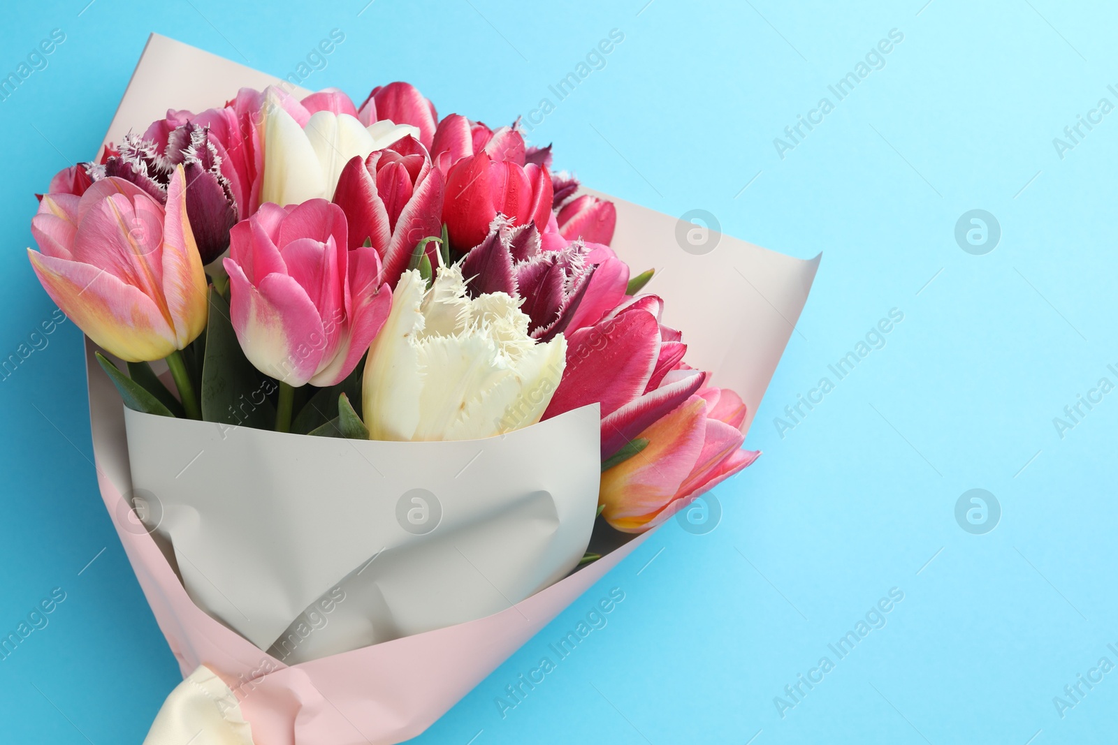 Bouquet of beautiful tulips on light blue background, top view. Space for text Photo of Bouquet of beautiful tulips on light blue background, top view. Space for text