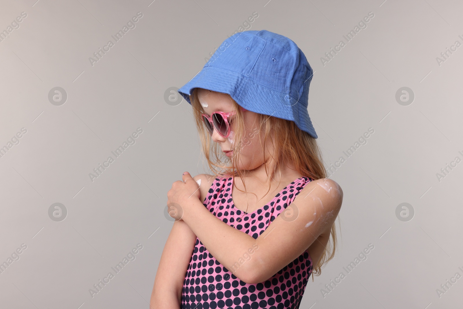 Cute little girl applying sun protection product onto her shoulder on grey background Photo of Cute little girl applying sun protection product onto her shoulder on grey background
